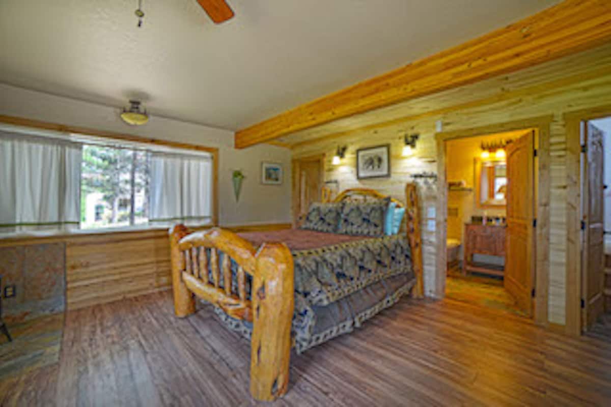 Ein Schlafzimmer in einer Blockhütte mit einem hölzernen Bett, einem Fenster mit Vorhängen und einem Deckenventilator.