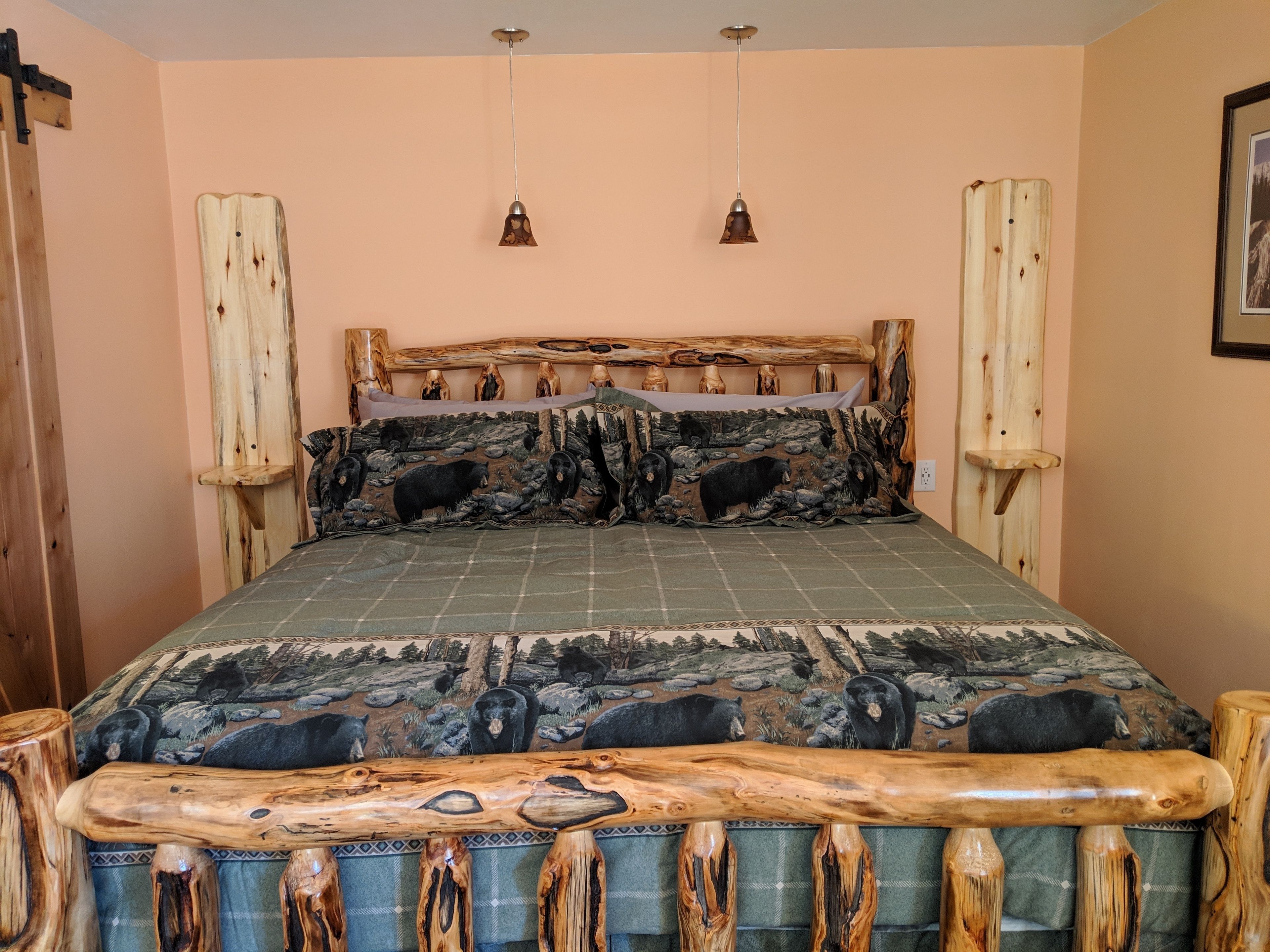 Un letto con testiera in legno, copriletto a tema foresta e due lampade a sospensione.