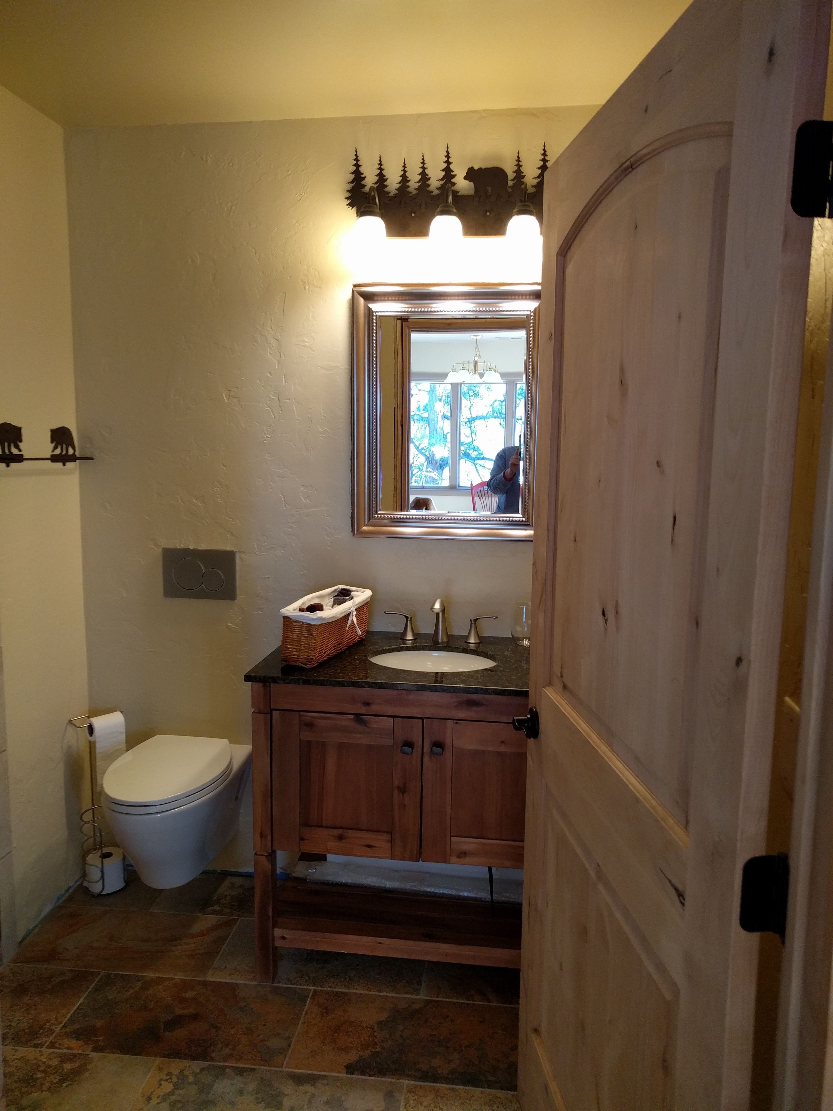 Une salle de bain avec un meuble-lavabo en bois, des toilettes blanches et un miroir doté d’un cadre décoratif.