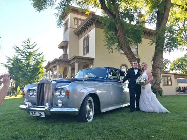 A vintage car parked in front of a building with a balcony and a tree.