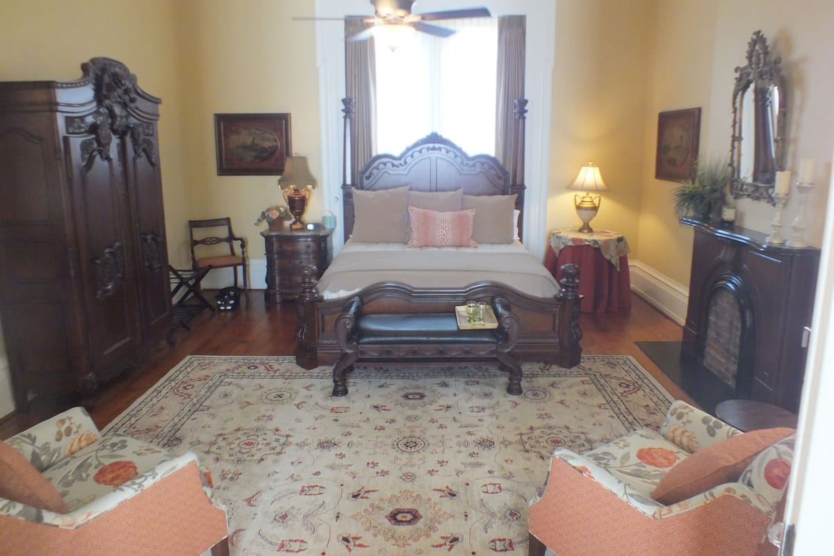 A traditional bedroom with a four-poster bed, a wooden floor, a patterned rug, and a classic chandelier.