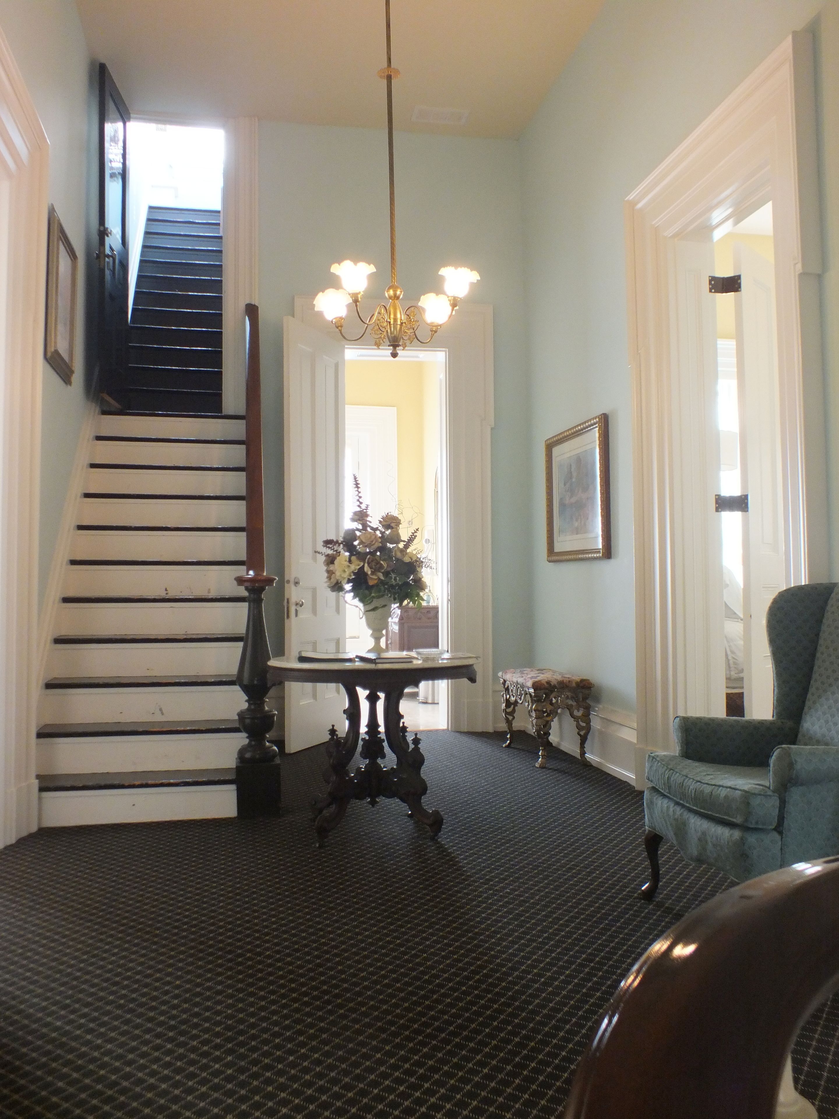 A staircase leading to a door, a chandelier, a table with a vase, and a chair.