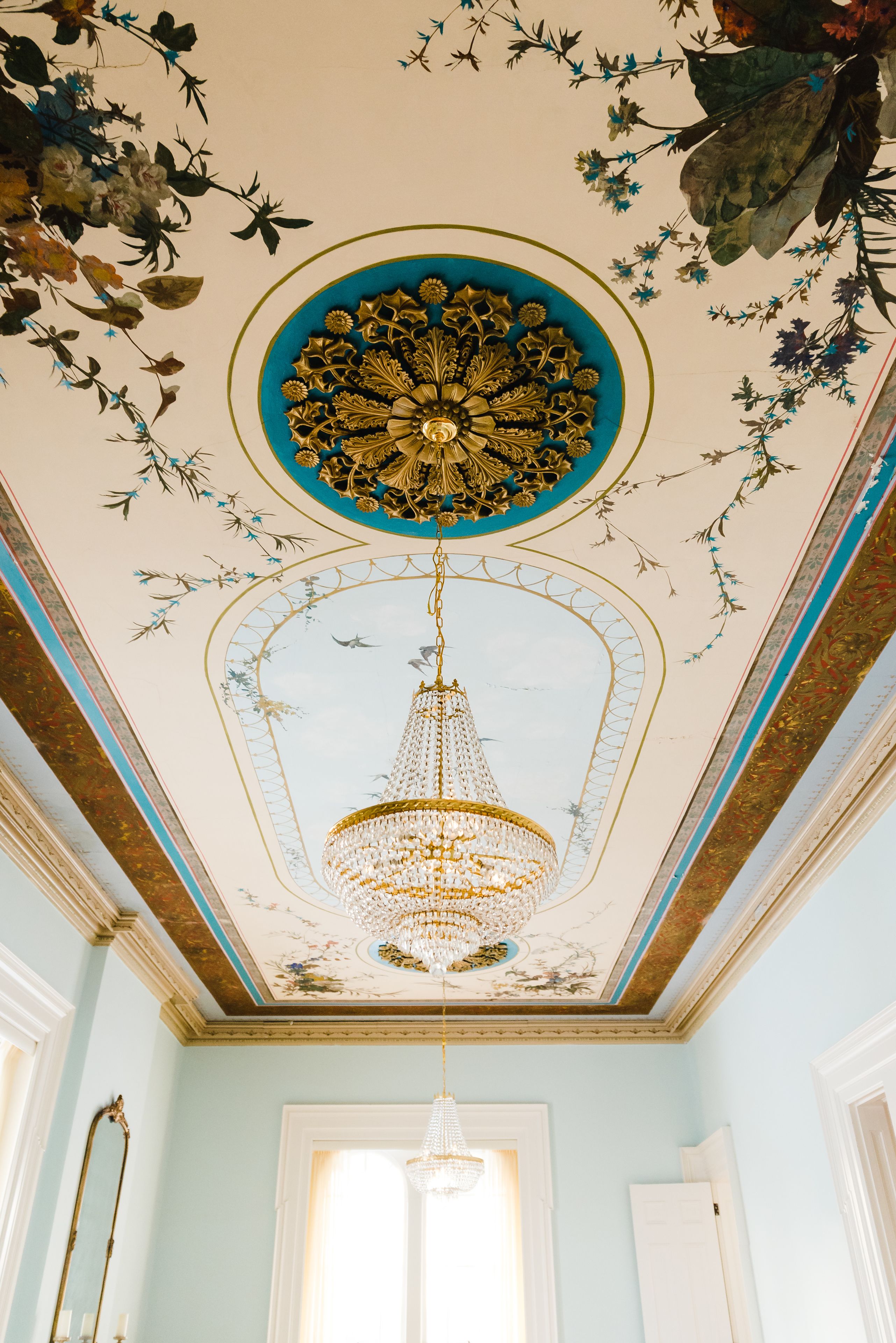 Una habitación con candelabro, diseño floral en el techo y una puerta.