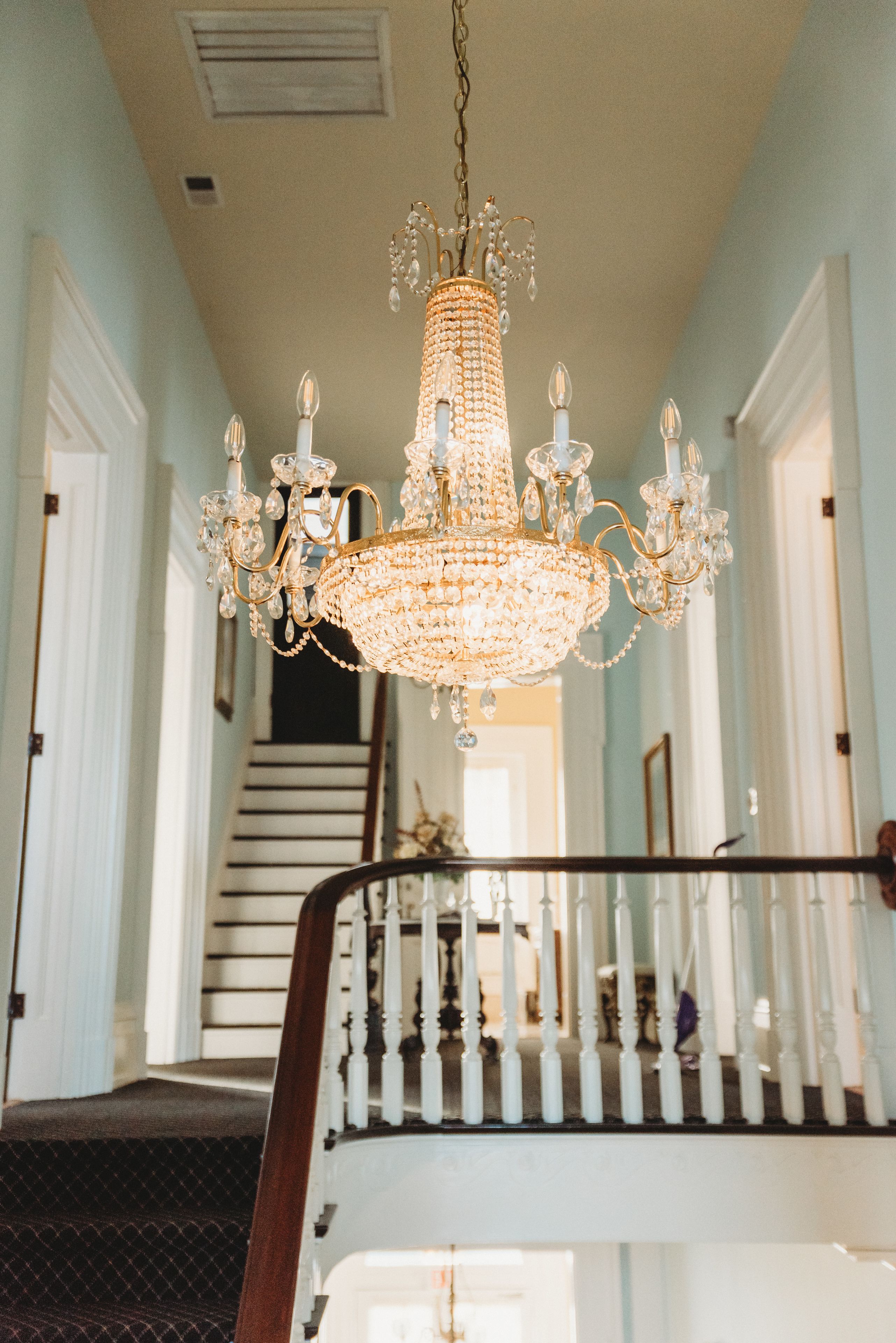 A grand chandelier hanging from the ceiling in a spacious hallway with a staircase.