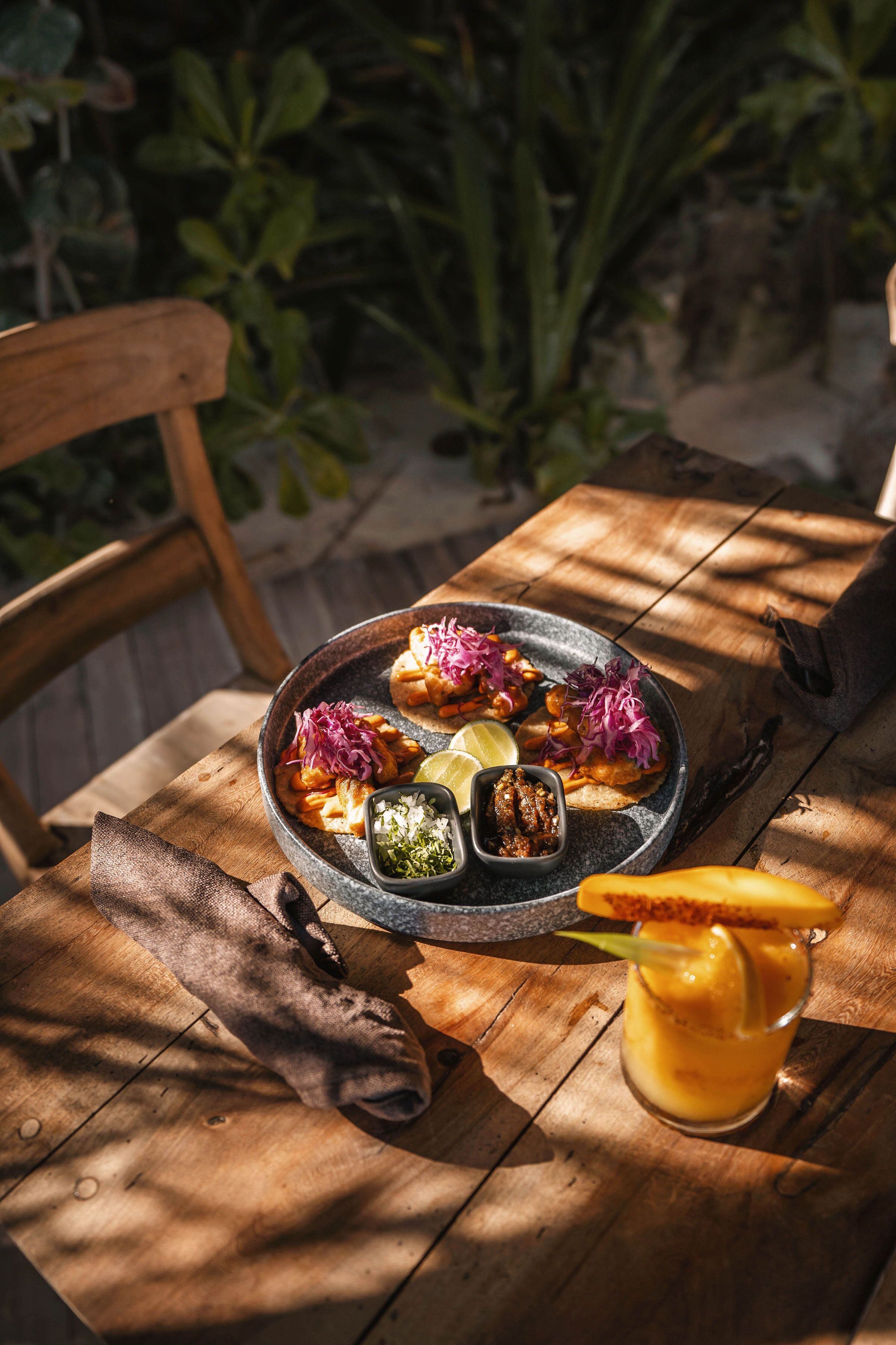 A wooden table with a plate of food, a glass of drink, and a napkin.