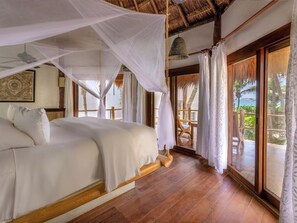 A bedroom with a bed, wooden floor, and a view of the outdoors.