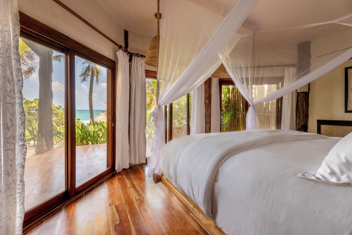 Un dormitorio con una cama grande, suelo de madera y vistas al océano a través de ventanas del suelo al techo.