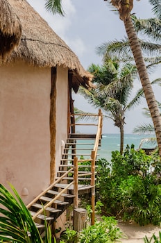Traditional thatched-roof structure with a staircase leading to an upper level, surrounded by lush tropical vegetation and a serene ocean view. at Encantada Tulum