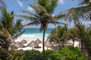 A beach with palm trees and thatched umbrellas.