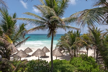 Relax on the pristine beach with unobstructed ocean views, shaded by thatched umbrellas and surrounded by palm trees. at Encantada Tulum