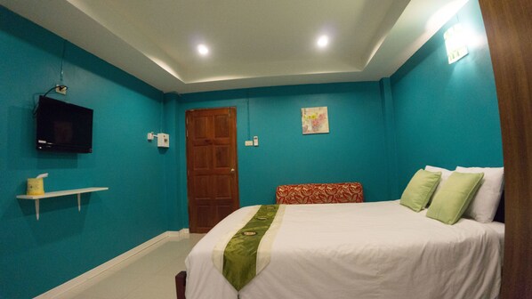 A bedroom with teal walls, a wooden door, a bed with green and white bedding, a TV on the wall, and a small shelf with a tissue box. - Weerawadee Place (Khon Kaen)