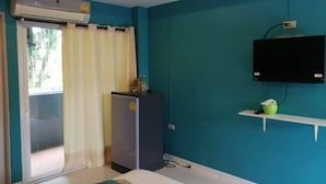 Una habitación con paredes color turquesa, una cama, un refrigerador pequeño, un televisor en un estante y una puerta corrediza a un balcón.