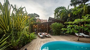 Un área junto a la piscina con sillones de descanso, una terraza de madera y un cartel que dice 'Selina'.