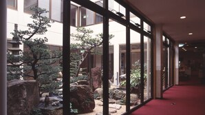 Un couloir doté d’un mur de verre derrière lequel se trouve un jardin de rochers et des bonsaïs.