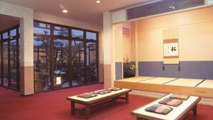 Une pièce de style japonais traditionnel, avec des tatamis, de petites tables basses en bois et une porte coulissante donnant sur un jardin.
