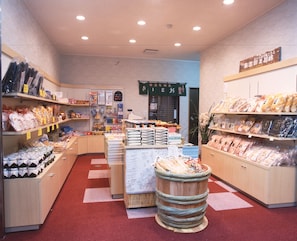 L’intérieur d’un magasin, avec des étagères remplies de divers produits emballés, une table centrale servant de présentoir et un tonneau en bois décoratif.
