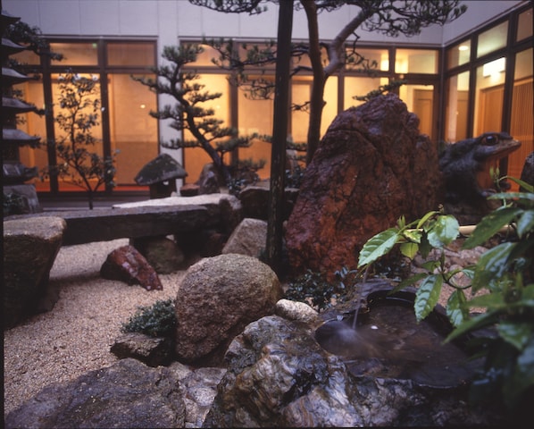 Un jardin japonais traditionnel, avec des rochers, un petit étang et des arbres bonsaï.