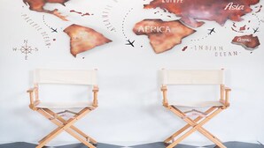 Two wooden director's chairs facing each other on a checkered floor with a world map in the background. - Sleep Cube (Khon Kaen)