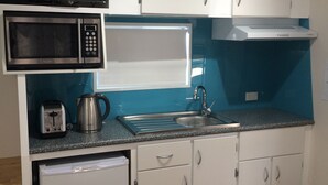 A compact kitchen with white cabinets, a microwave, a toaster, a kettle, and a sink. - Riviera Caravan Park (Sussex Inlet)