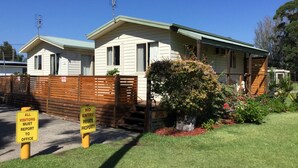 A single-story house with a green roof, a fenced yard, and a sign indicating it is private property. - Riviera Caravan Park (Sussex Inlet)
