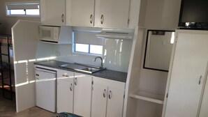 A compact kitchen with white cabinets, a microwave, a sink, and a refrigerator. - Riviera Caravan Park (Sussex Inlet)