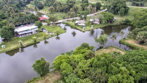 Une vue aérienne d’une propriété riveraine, avec une petite maison, un bâtiment plus grand doté d’un toit rouge et une jetée qui s’avance dans l’eau.
