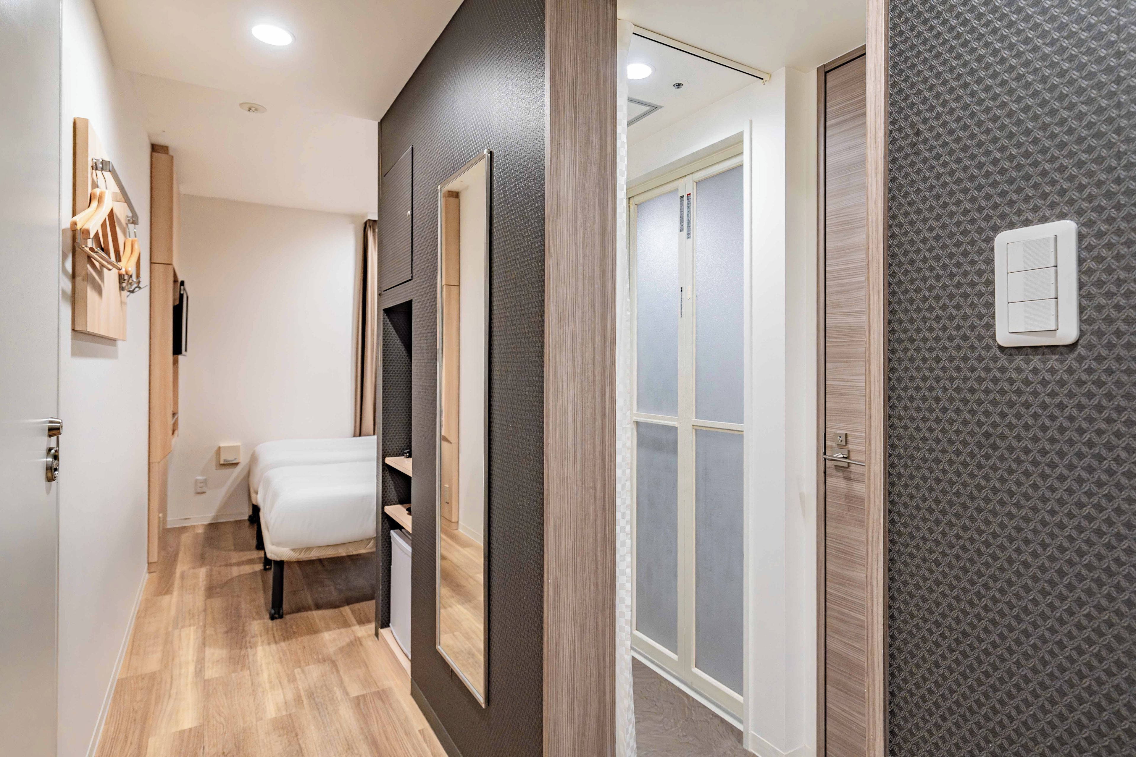 A hotel room with a bed, a wardrobe, a mirror, and a door leading to another room.