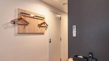 A hotel room with a wooden coat rack, a door, and a small table with a tissue box and a clock.