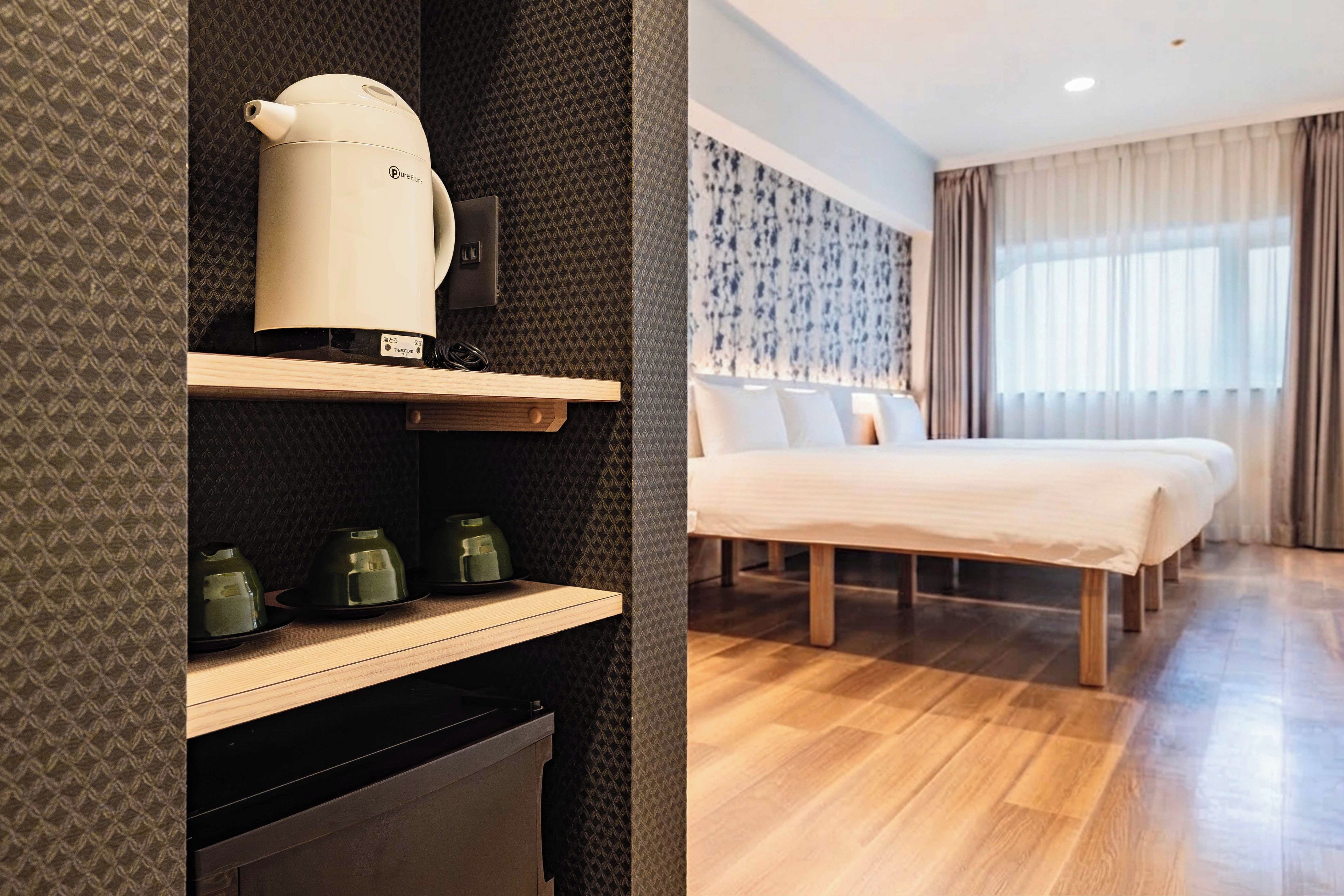 Una habitación de hotel con una cama, un estante con un hervidor y un pequeño electrodoméstico.