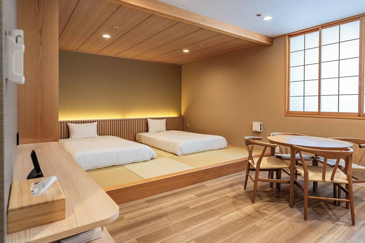 Ein Hotelzimmer mit zwei Betten, einem Holztisch und einem großen Fenster.