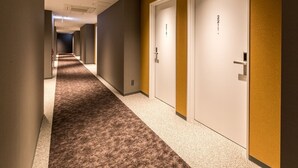 Un pasillo de hotel con pisos alfombrados, puertas blancas con números de habitación y un diseño moderno.
