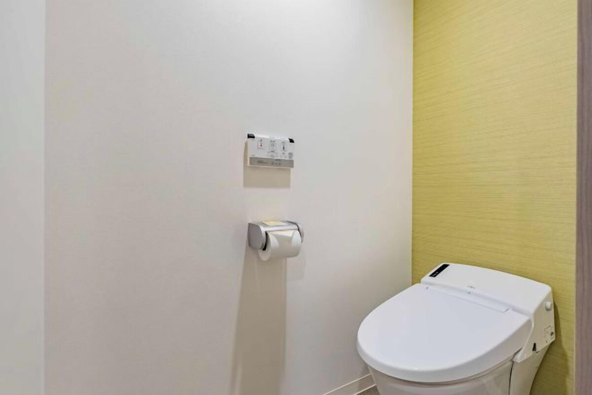 A bathroom with a toilet, a paper towel dispenser, and a wall-mounted electrical outlet.