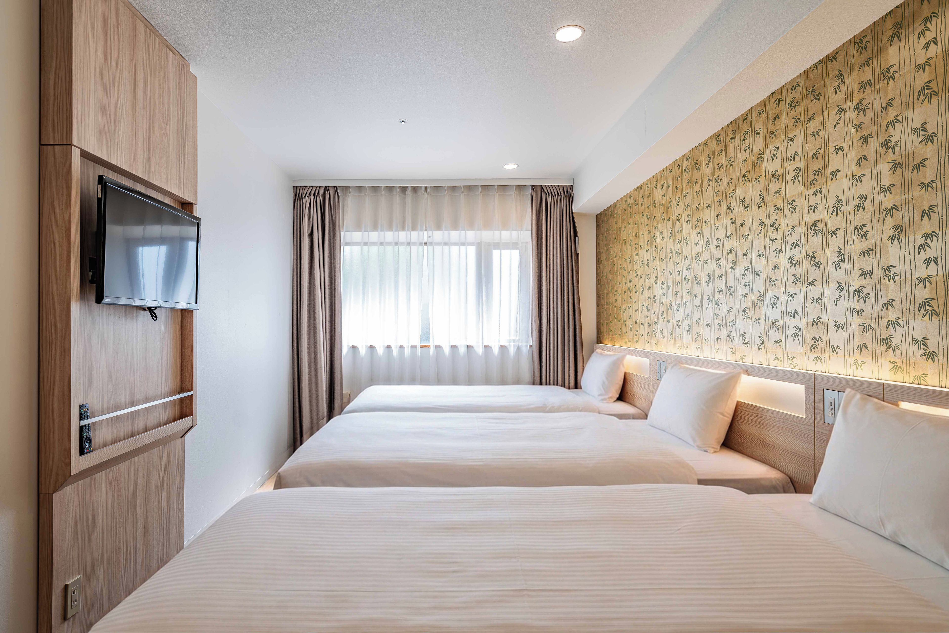 A hotel room with two beds, a TV, and a wall with a bamboo pattern.