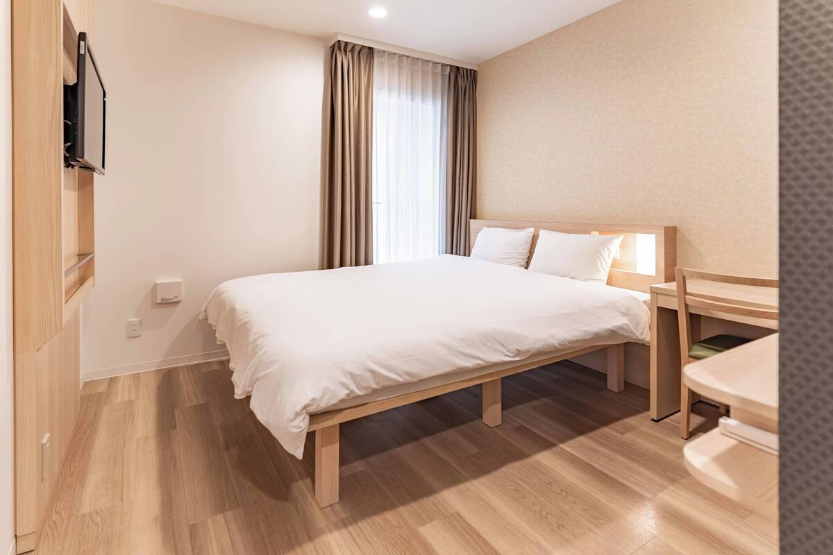 Ein Hotelzimmer mit einem großen Bett, einem Nachttisch, einem Schreibtisch und einem an der Wand befestigten Fernseher.