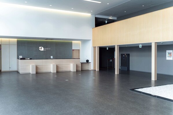 A modern hotel reception area with a reception desk, a waiting area, and a staircase leading to an upper level.