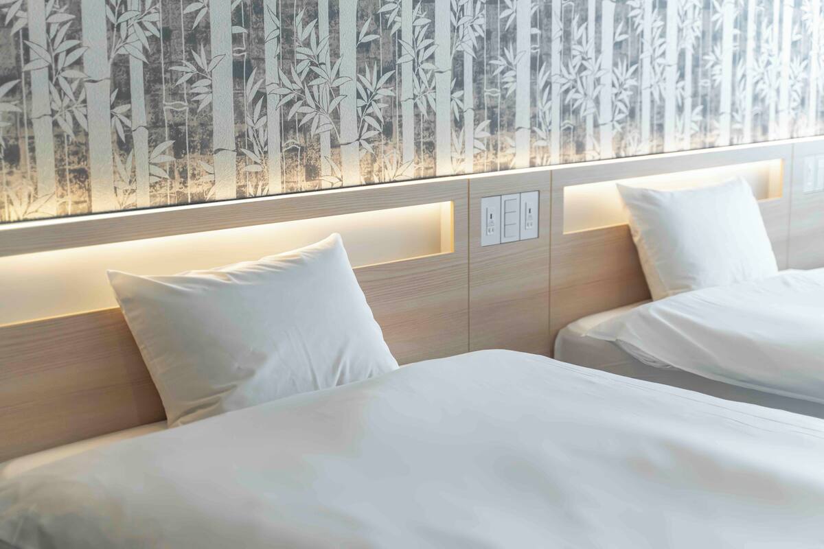 Ein Hotelzimmer mit zwei Betten, einem Kopfteil mit integrierter Beleuchtung und einer Wand mit Bambusmuster.