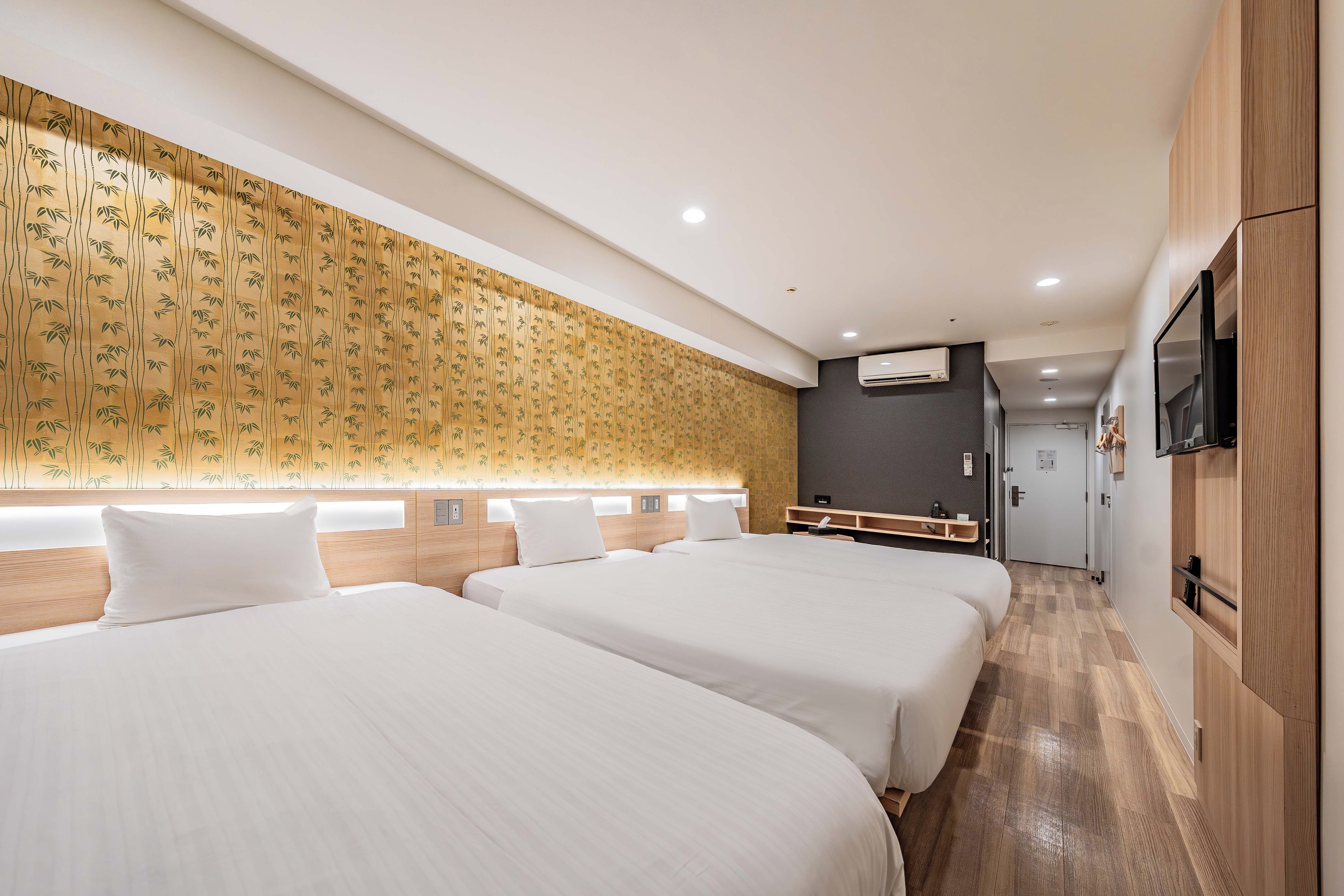 A hotel room with two beds, a wall-mounted TV, and a wooden floor.
