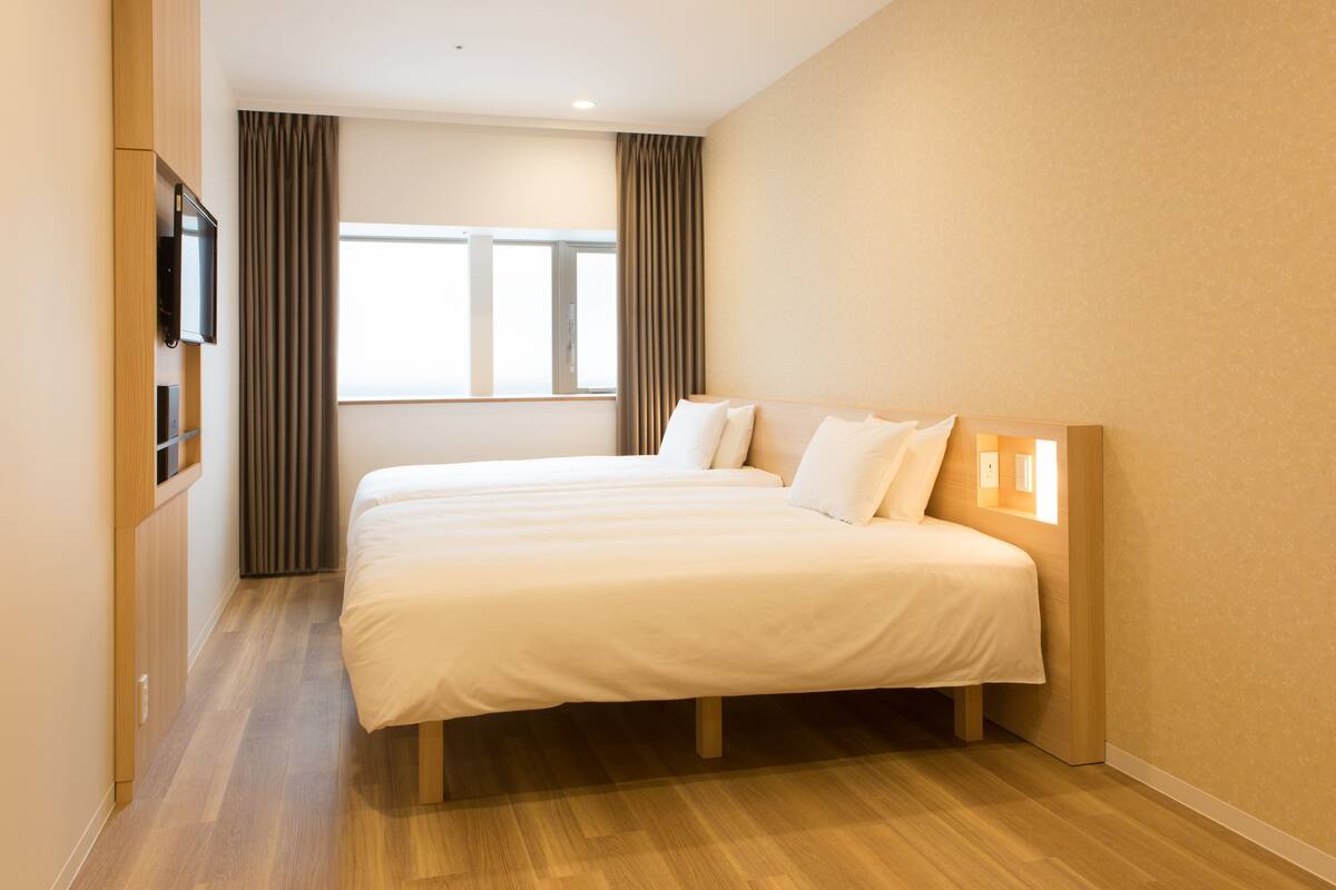 Ein Hotelzimmer mit einem großen Bett, Holzboden, einem an der Wand montierten Fernseher und einem Fenster mit Vorhängen.