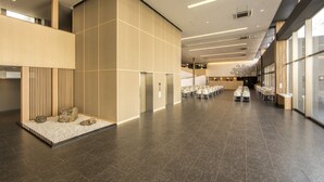 Eine geräumige Lobby mit hoher Decke, moderner Beleuchtung und einer Sitzecke mit Tischen und Stühlen.