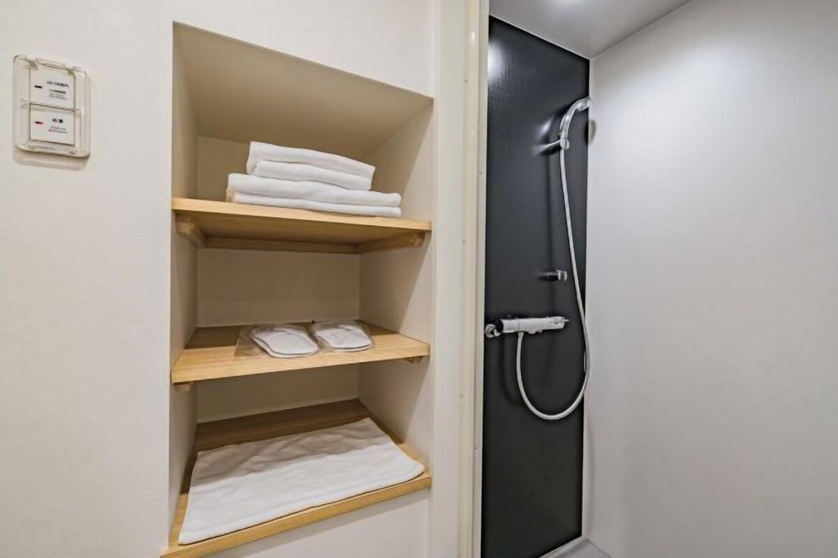 A bathroom with a black door, a shower, and wooden shelves with towels.