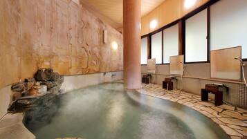 Relax in a serene hot spring bath area featuring a central hot spring surrounded by stone steps and individual tubs with privacy screens.