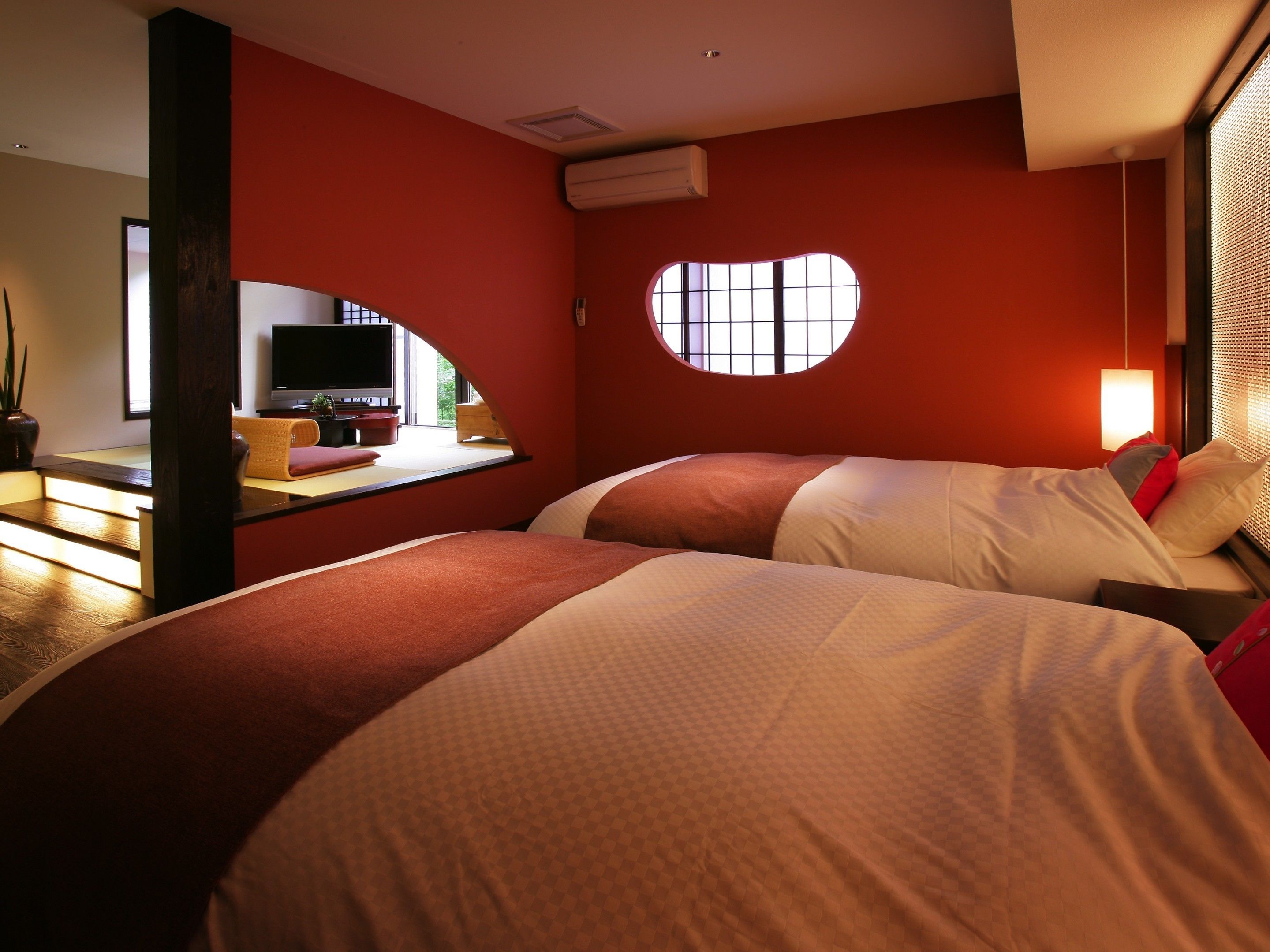 A hotel room with two beds, a desk with a TV, and a window with a view.