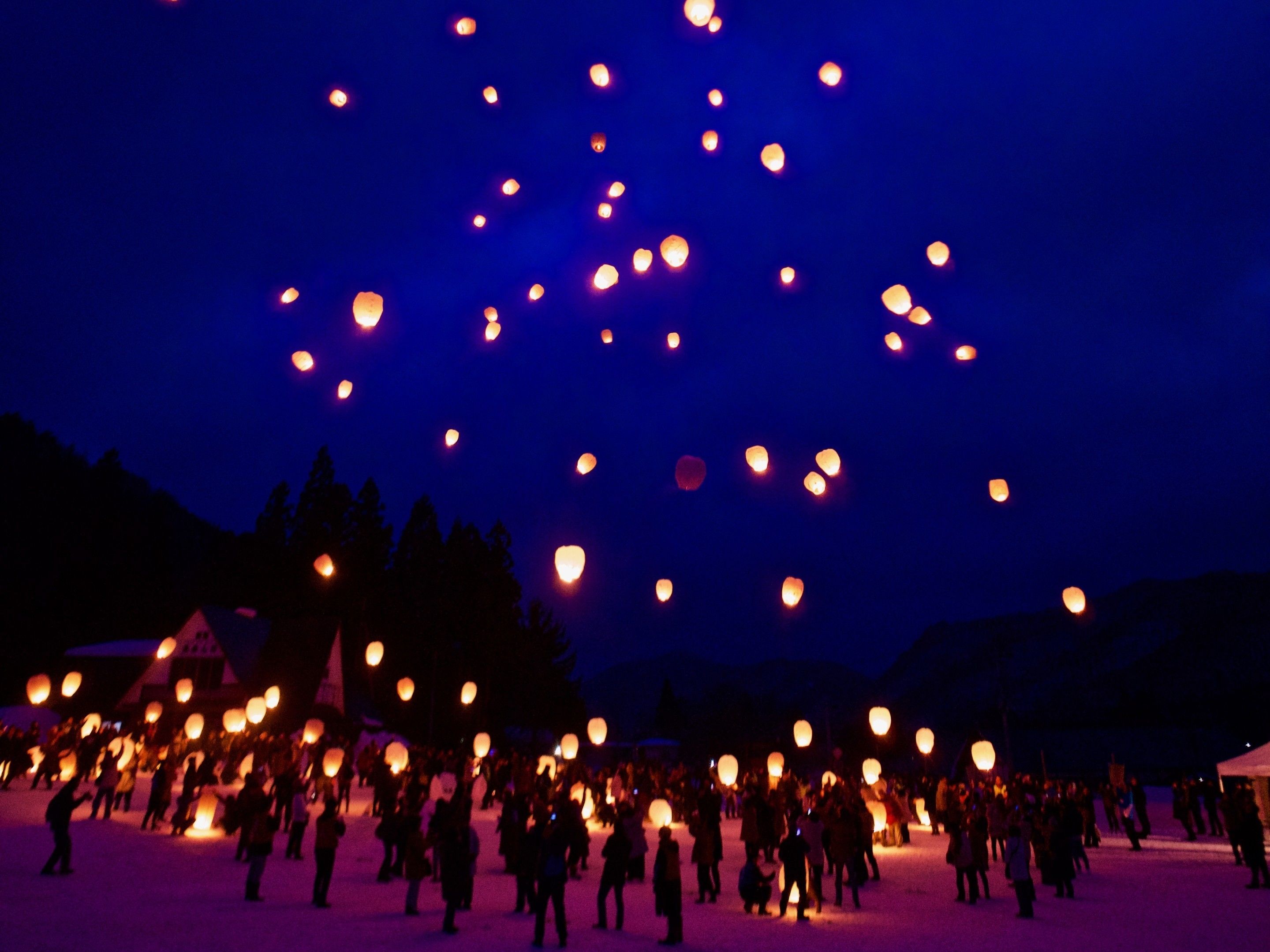 A large open space with a crowd of people and numerous floating lanterns.