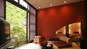 Habitación de hotel moderna con un televisor grande, un sofá, una mesita con juego de t é y vistas a zonas verdes.