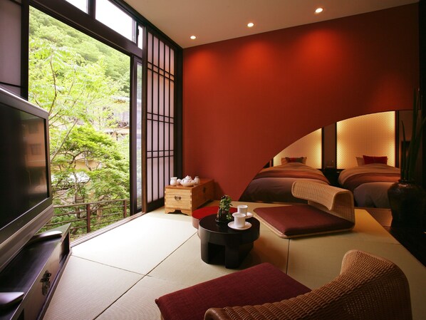 Habitación de hotel moderna con un televisor grande, un sofá, una mesita con juego de té y vistas a zonas verdes.