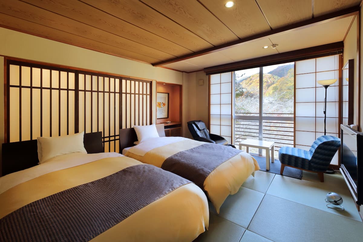 Ett hotellrum med två sängar, en traditionell japansk skjutdörr, ett skrivbord, en stol och utsikt över omgivningarna.