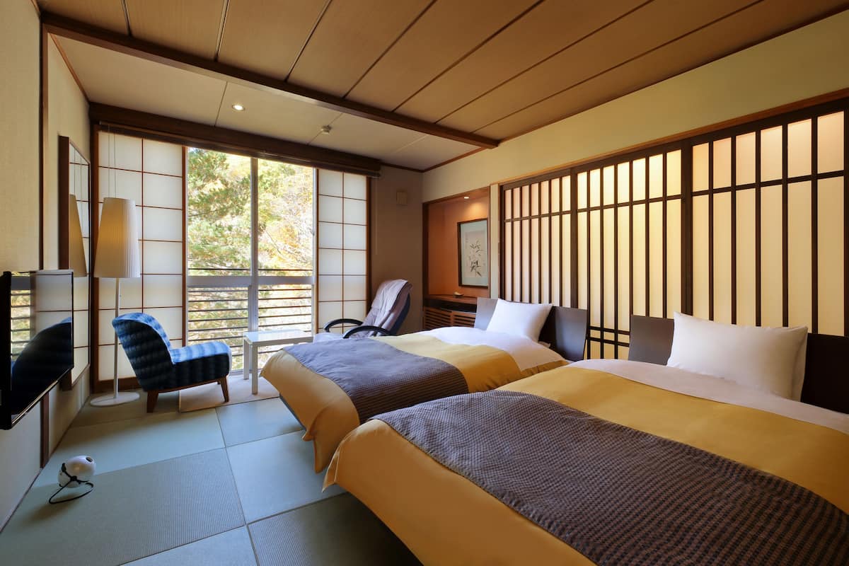 Ett hotellrum med tatamimattor på golvet, en traditionell japansk säng, ett skrivbord och en stol.