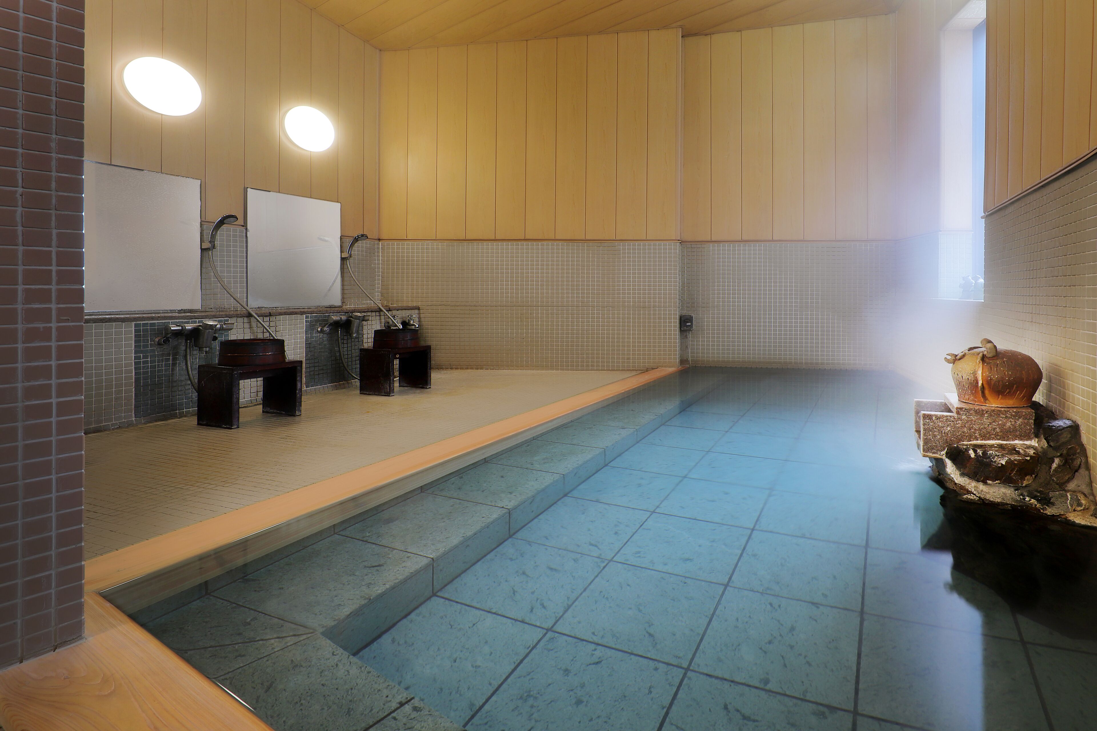 Ein öffentlicher Badebereich mit Holzwänden, Fliesenböden und einem zentralen Pool.