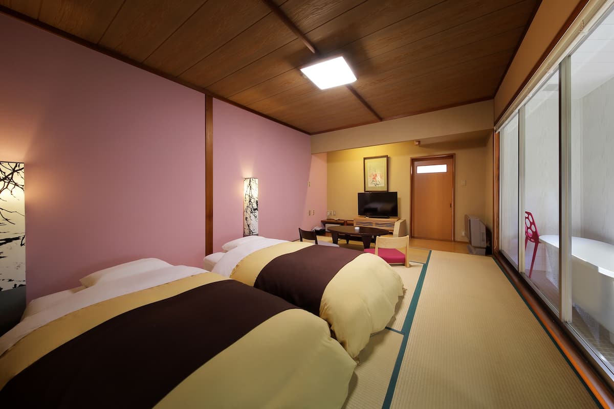 Ett hotellrum med två sängar, en tv och en skjutdörr som leder ut till en balkong.