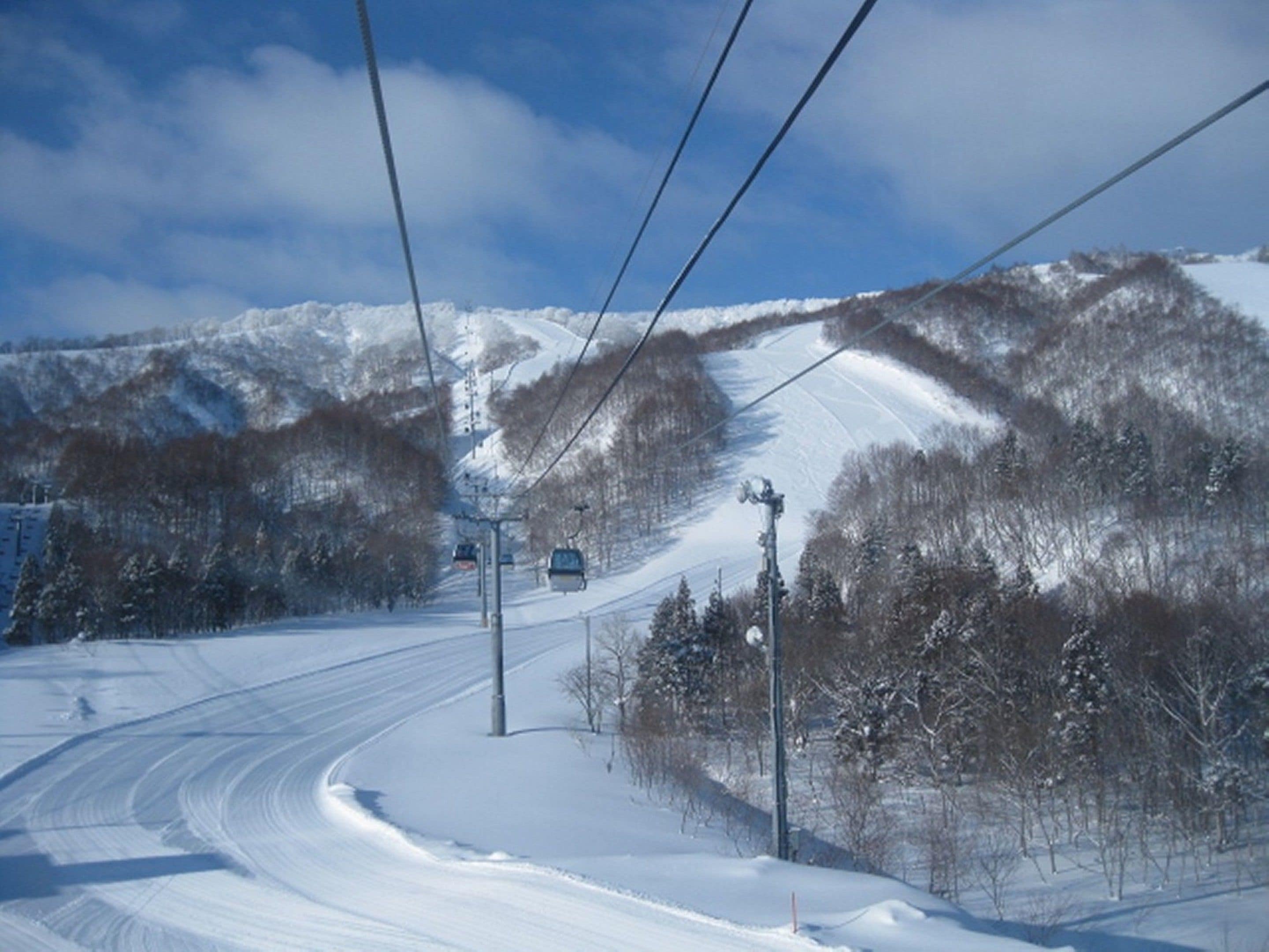 A snowy mountain road with a ski lift and power lines.